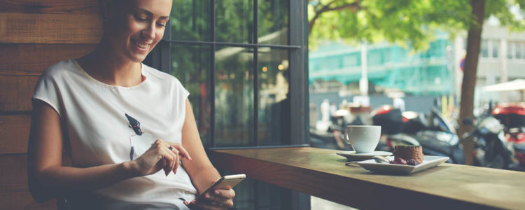 woman with beautiful smile reading good news on mobile phone during rest in coffee shop