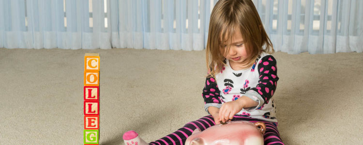 young girl on the floor with a piggy bank and blocks arranged to spell college